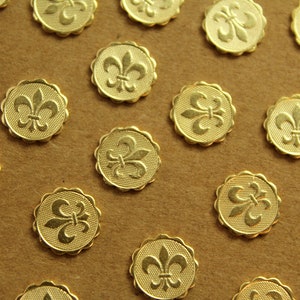 May include: Gold-colored metal buttons with a fleur-de-lis design. Each button has a scalloped edge and a textured surface. The buttons are scattered on a brown surface.