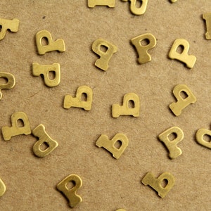 May include: A close-up of a brown surface covered with gold-colored metal letter 'P' charms.