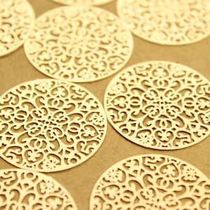 May include: A collection of round, decorative, laser-cut paper doilies with a delicate, intricate floral pattern. The doilies are a pale gold color and have a slightly textured surface.