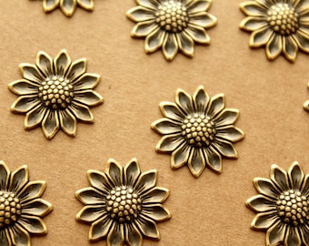 May include: A collection of gold-toned metal sunflower embellishments with a textured finish. The sunflowers are arranged on a brown background.