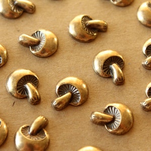 May include: A collection of gold-toned metal mushroom-shaped decorative accents. The mushrooms have a detailed design and are arranged on a brown surface.