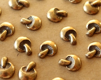 May include: A collection of gold-toned metal mushroom-shaped decorative accents. The mushrooms have a detailed design and are arranged on a brown surface.