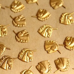 May include: A collection of gold-toned metal unicorn head charms with a raised design. The charms are scattered on a brown surface.