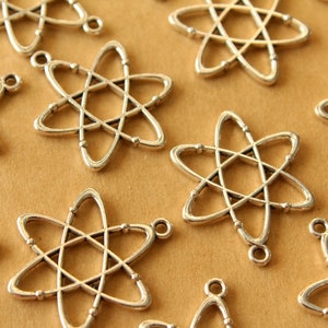 May include: A group of silver-toned metal charms shaped like an atom. The charms have a loop at the top for attaching to a necklace or bracelet.