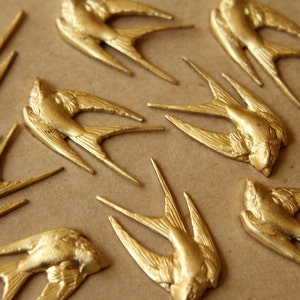 May include: A collection of gold-colored metal swallow bird figurines. The birds are arranged in a scattered pattern on a brown surface.