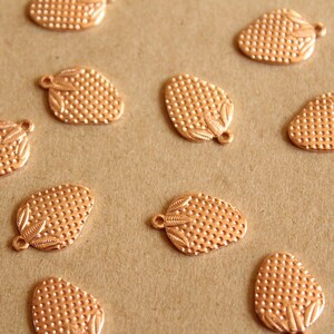 May include: A collection of 12 copper-coloured metal charms shaped like strawberries. Each charm has a textured surface and a small loop for attaching to a necklace, bracelet, or other jewellery.