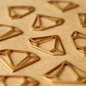 May include: A collection of gold-coloured metal diamond-shaped cutouts on a brown surface. The cutouts are geometric and have a delicate, intricate design.
