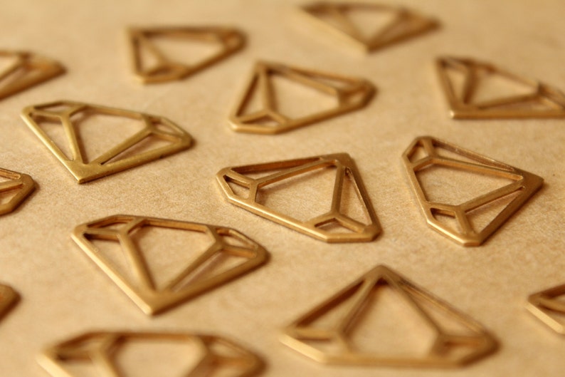 May include: A collection of gold-coloured metal diamond-shaped cutouts on a brown surface. The cutouts are geometric and have a delicate, intricate design.