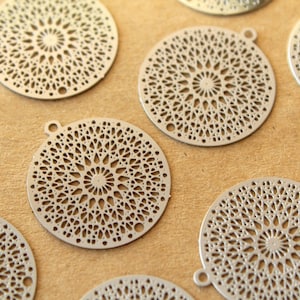 May include: A set of eight silver metal round decorative charms with intricate laser cut designs. The charms have a circular shape with a delicate pattern of geometric shapes and lines.