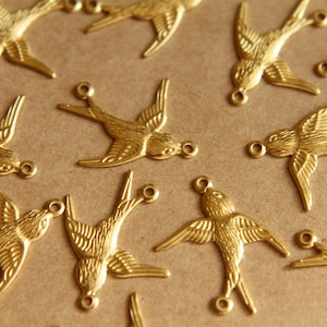 May include: A collection of gold-toned metal swallow charms with a detailed design. The charms have a loop at the top for attaching to jewelry or other crafts.