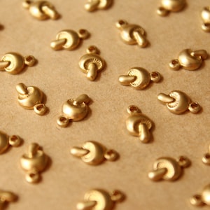 Puede incluir: Una colección de abalorios con forma de hongo de color dorado. Los abalorios tienen un diseño detallado y son perfectos para añadir un toque de fantasía a las joyas o las manualidades.