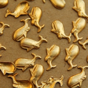 May include: A collection of gold-colored whale-shaped metal charms. The charms are all the same size and shape, and they have a detailed design.