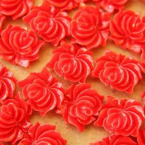 May include: A close-up of a group of bright red plastic rose-shaped embellishments. The roses are arranged in a random pattern on a brown surface.