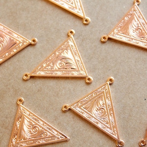 Peut inclure: Huit breloques en métal de forme triangulaire dorées avec un motif floral complexe. Chaque breloque a trois trous pour l'attacher à un collier, un bracelet ou un autre bijou.
