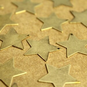 Peut inclure: Une collection d'&eacute;toiles en m&eacute;tal dor&eacute; &eacute;parpill&eacute;es sur une surface brune. Les &eacute;toiles sont de diff&eacute;rentes tailles et ont une finition l&eacute;g&egrave;rement textur&eacute;e.