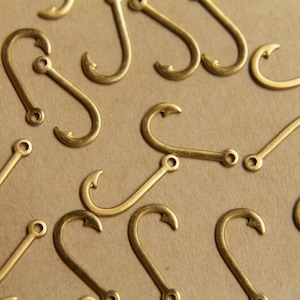 May include: A collection of gold-toned metal hooks, scattered on a brown surface. The hooks are all the same size and shape, with a simple, curved design.