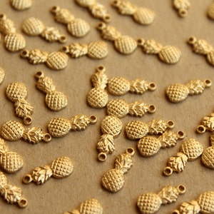 May include: A large group of gold pineapple charms, each with a textured surface and a loop for attaching to a necklace or bracelet.