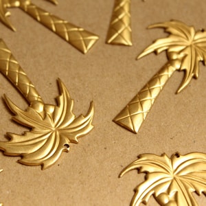 May include: A collection of gold-toned metal palm tree ornaments. The ornaments are detailed with a textured trunk and intricate palm fronds.