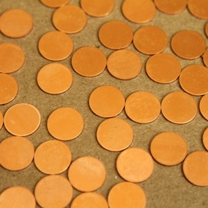 May include: A close-up image of a large quantity of small, round, copper-colored discs. The discs are arranged in a random pattern on a brown surface.