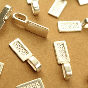 Może przedstawiać: Srebrne metalowe zawieszki do zawieszek w kształcie prostokąta z fakturowaną powierzchnią. Zawieszki mają pętelkę u góry do przymocowania łańcuszka lub sznurka.