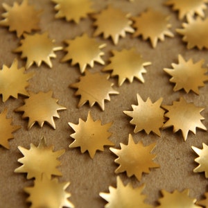 May include: A close-up of a large quantity of gold-colored star-shaped metal embellishments. The stars are scattered on a brown surface.