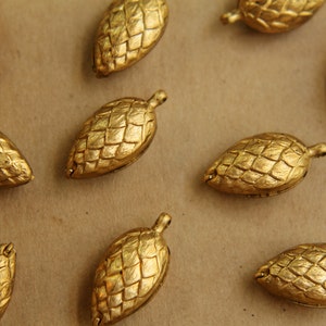 May include: A collection of ten gold-coloured pine cone shaped ornaments. The ornaments are all different sizes and have a textured surface.