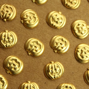 May include: A close-up of a collection of gold-colored metal pumpkin-shaped buttons. The buttons have a carved design and are arranged in a grid pattern on a brown surface.