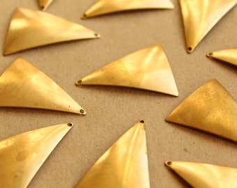 Può includere: Un gruppo di ciondoli in metallo dorati a forma di triangolo con un foro nella parte superiore. I ciondoli sono sparsi su una superficie marrone.