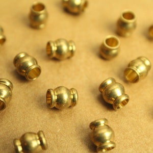 May include: A collection of 17 gold-colored metal beads, each with a rounded shape and a smooth surface. The beads are arranged on a brown surface.