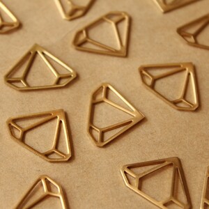 May include: A collection of gold-coloured metal diamond shapes, scattered on a brown surface. Each diamond has a geometric design.