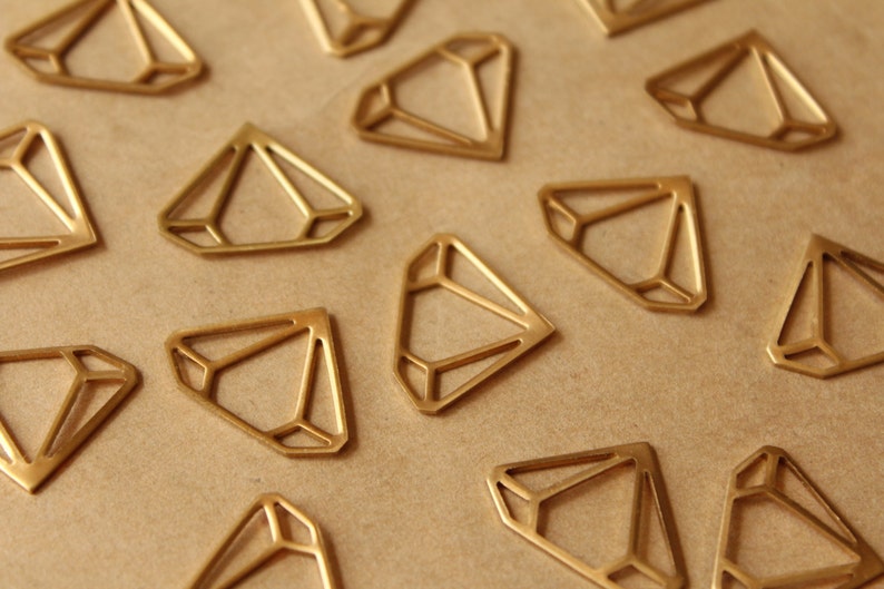 May include: A collection of gold-coloured metal diamond shapes, scattered on a brown surface. Each diamond has a geometric design.