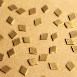 Pode incluir: Uma coleção de pequenas peças de metal em forma de diamante, de cor dourada, espalhadas sobre uma superfície marrom.