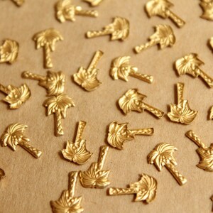 May include: A scattering of gold-toned palm tree charms on a brown surface. The charms are detailed with a textured palm tree design.