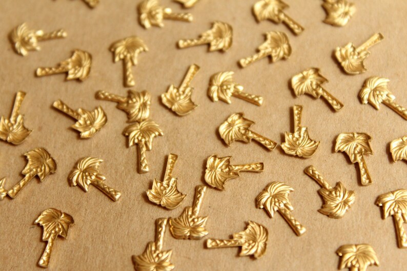 May include: A scattering of gold-toned palm tree charms on a brown surface. The charms are detailed with a textured palm tree design.