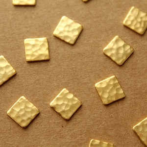 May include: A collection of gold-colored, hammered metal squares. The squares are arranged in a pattern on a brown surface.