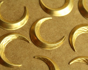 May include: A collection of gold-colored crescent moon-shaped metal charms. The charms have a textured surface and are arranged on a brown background.