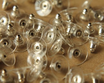 May include: A close-up of a pile of clear plastic earring backs with silver metal posts. The backs are designed to be used with stud earrings.