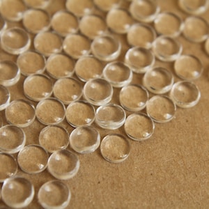 May include: A close-up of a group of clear, round, plastic beads scattered on a brown surface.