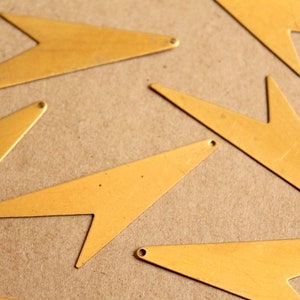 May include: A collection of gold-coloured metal arrow shapes, scattered on a brown surface. The arrows are all pointed in different directions.