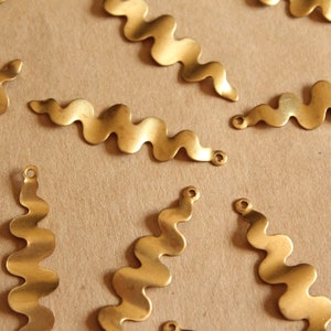 May include: A collection of gold-colored metal wavy shapes with small holes at the ends. The shapes are scattered on a brown surface.