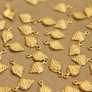 May include: A collection of gold-toned metal charms shaped like bunches of grapes. Each charm has a loop at the top for attaching to jewellery or other crafts.