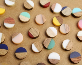 Op de afbeelding: Assortiment van ronde houten en harsversieringen in verschillende kleuren en patronen. Elk ornament is in tweeën gedeeld, met een helft van hout en de andere helft van hars.