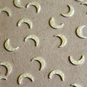 May include: A close-up of a brown surface covered with silver crescent moon charms. The charms are scattered randomly across the surface.