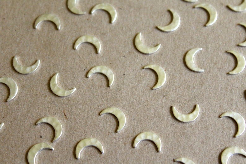 May include: A close-up of a brown surface covered with silver crescent moon charms. The charms are scattered randomly across the surface.