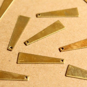 May include: A collection of ten brass triangle-shaped pendants with a hole at the top. The pendants are arranged on a brown surface.