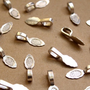 Peut inclure: Une collection de bélières de pendentif en métal argenté, chacune avec un motif ovale décoratif. Les bélières sont conçues pour être utilisées pour attacher des pendentifs à des chaînes ou des cordons de bijoux.