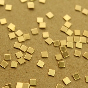 Könnte beinhalten: Eine Streuung kleiner, quadratischer, goldfarbener Metallstücke auf einer braunen Oberfläche.