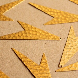 May include: A group of gold-coloured metal arrow shapes with a hammered texture. The arrows are arranged in a random pattern on a brown surface.