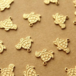 May include: A collection of gold-toned turtle charms with detailed etching. The charms have a loop at the top for attaching to jewelry or other crafts.