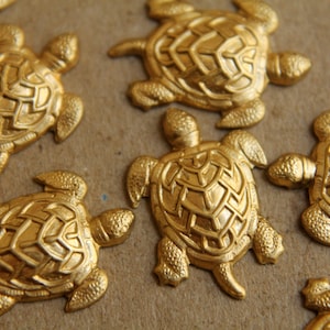 May include: A collection of gold-colored turtle figurines. The turtles are arranged in a random pattern on a brown surface.